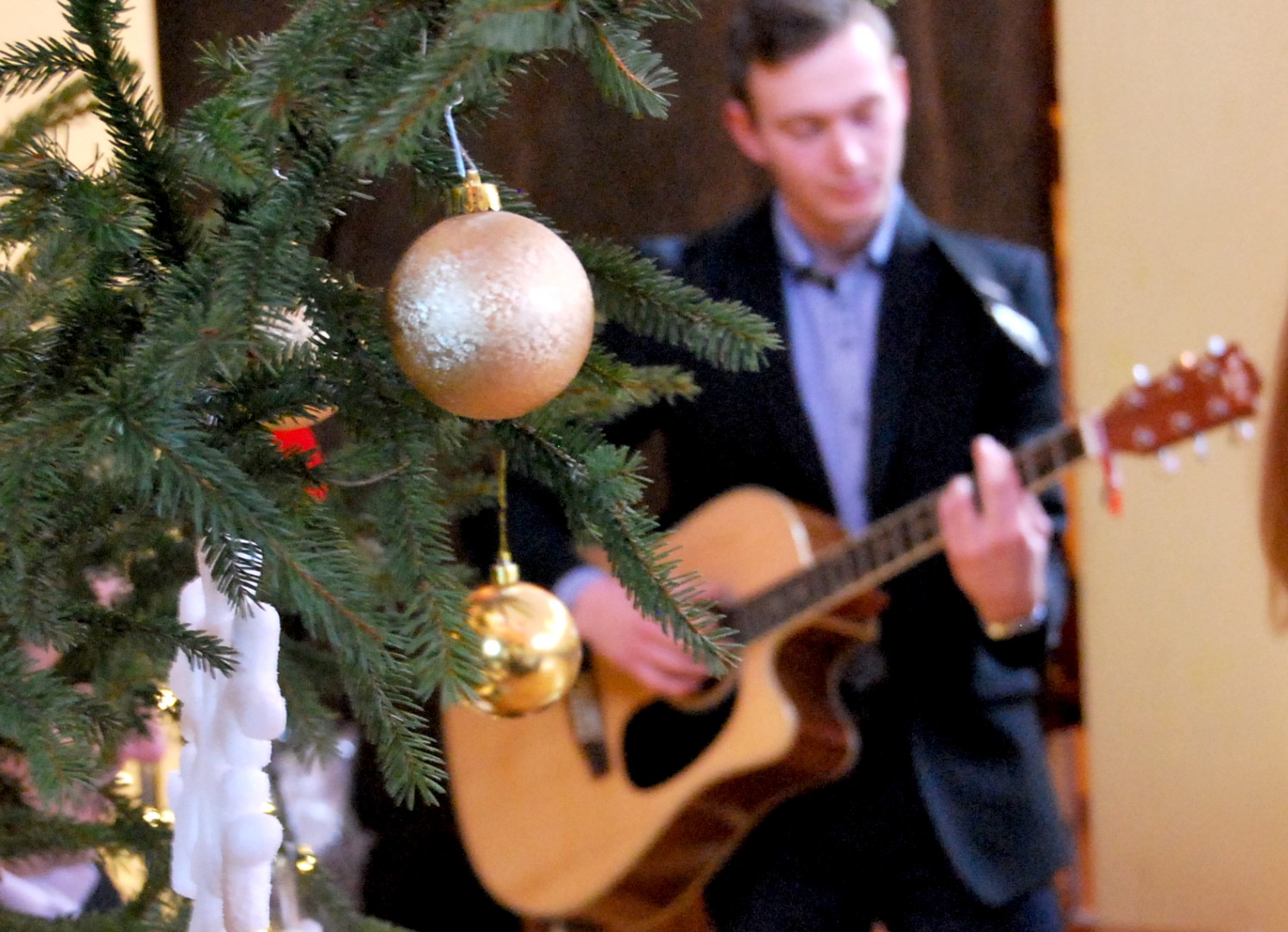 zdjęcie przedstawia pana grającego na gitarze i choinkę bożonarodzeniową na pierwszym planie